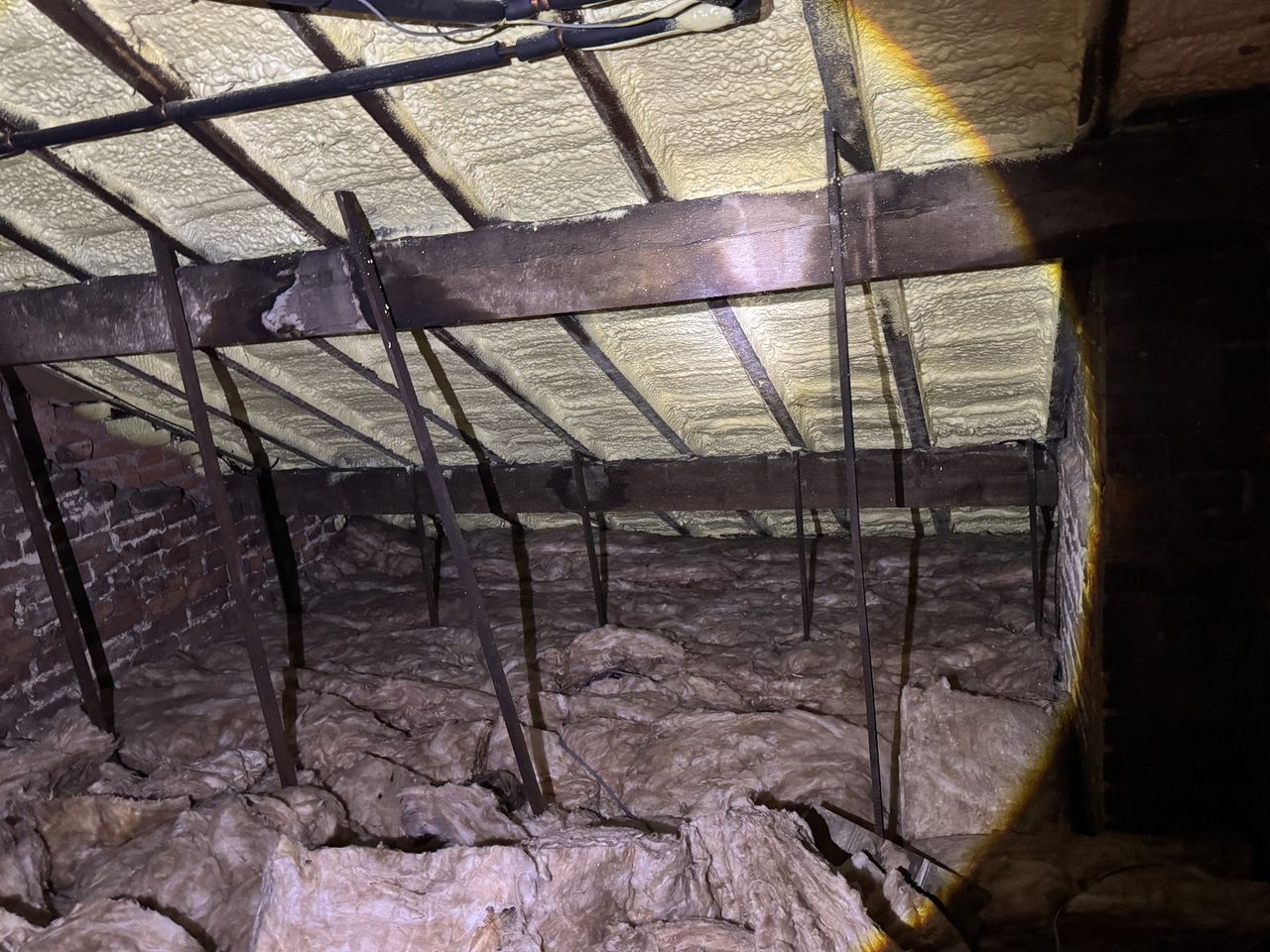 Independent spray foam inspection — closed-cell spray foam applied to the underside of the roof covering rafters and felt, with mineral-wool insulation at ceiling level