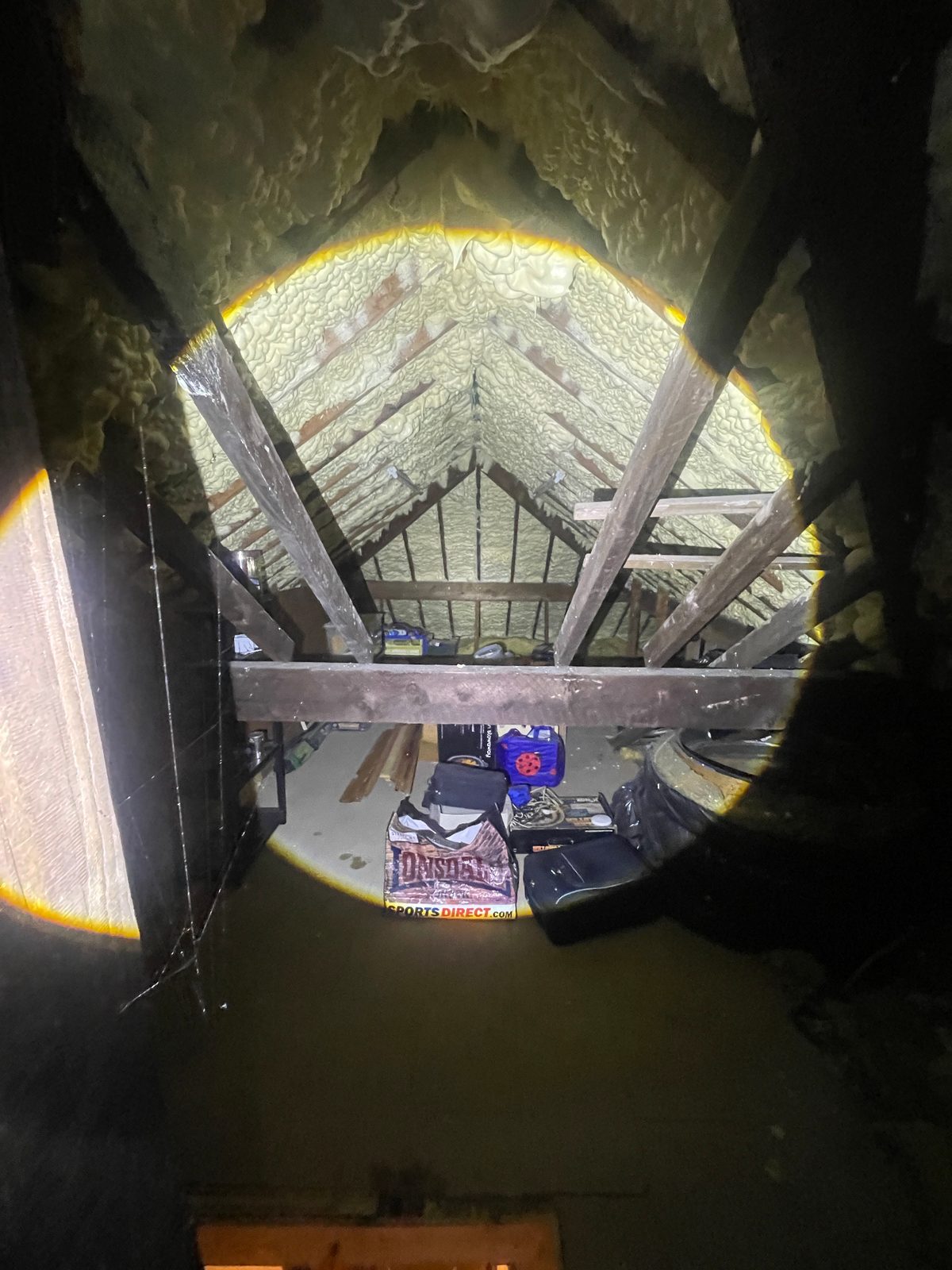 Independent spray foam loft inspection — wide view of a pitched roof void fully coated in spray foam, inspected with a torch to document coverage and access