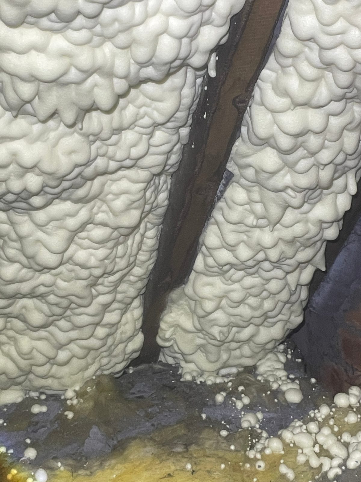 Independent spray foam loft inspection — close-up of closed-cell spray foam encapsulating a rafter, with uneven coverage and drips at the wall plate